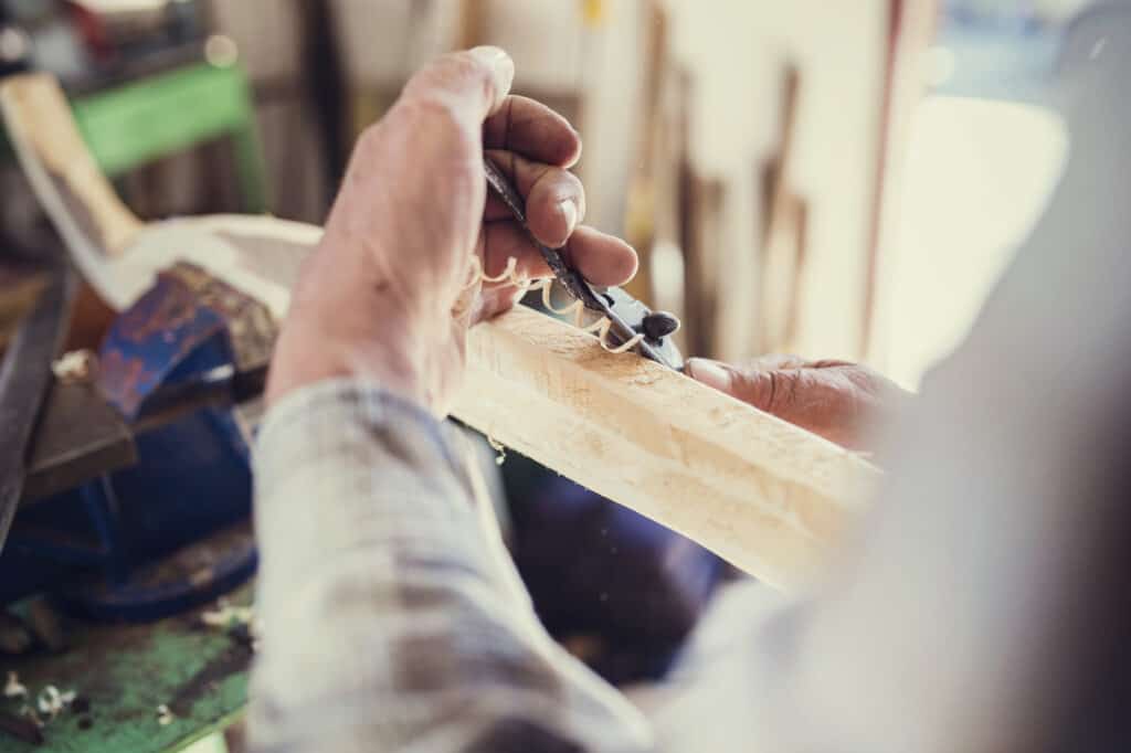 Senior craftsman working with planer on wooden pole in his workshop